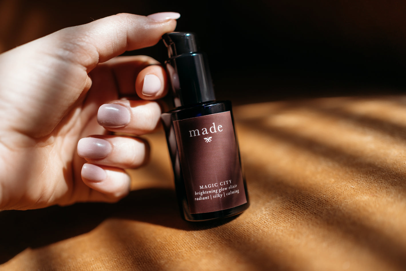 Hand on black skincare bottle for Made clean skincare line and Magic City brightening vitamin C Oil.